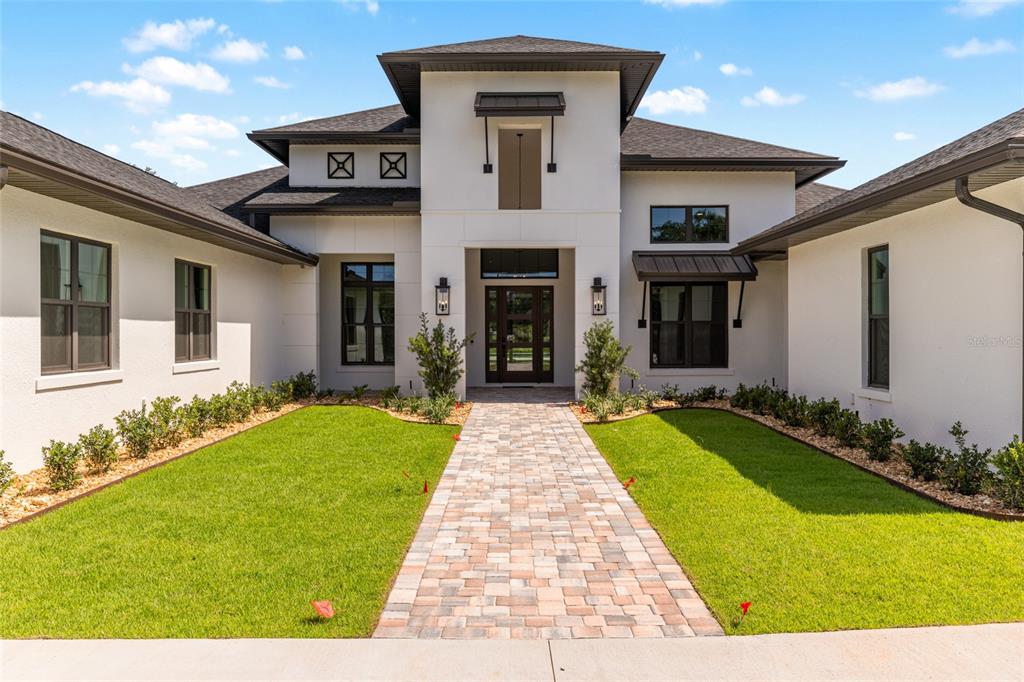 A modern white house with a dark roof and a brick walkway leading to the entrance — 950 SE 80TH STREET, OCALA, FL