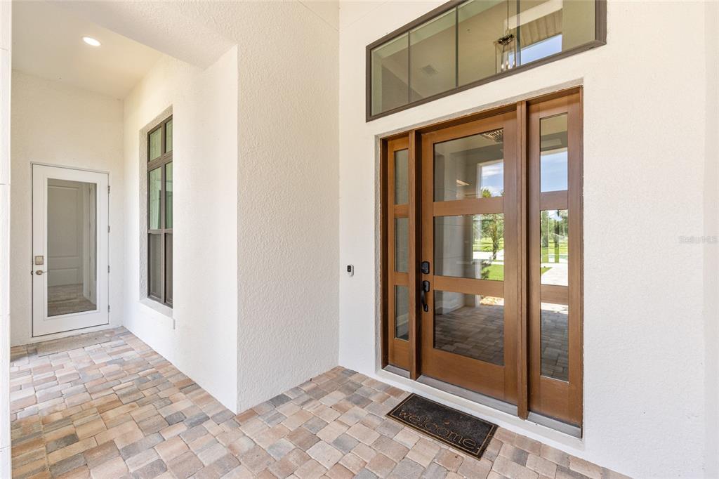 A modern entryway features a wood-framed glass front door, sidelights, and a stone paver porch — 950 SE 80TH STREET, OCALA, FL