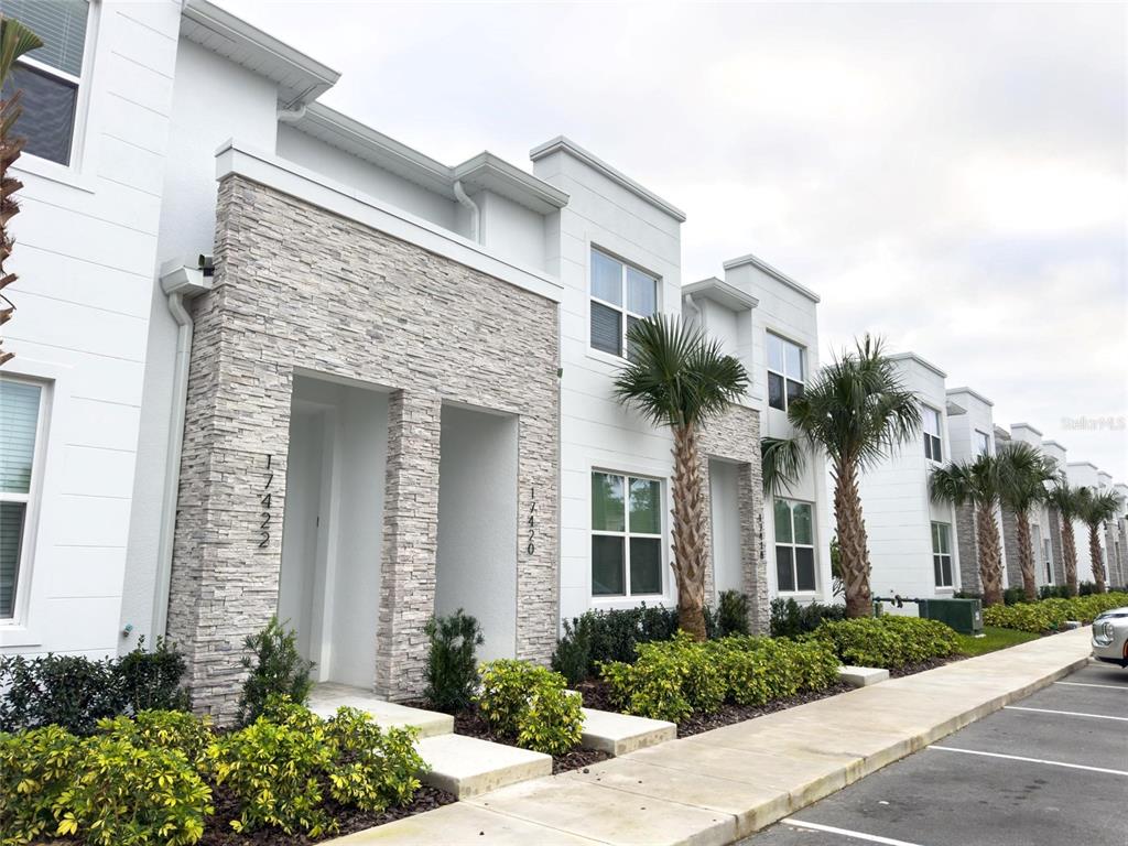 A row of modern townhomes features white stucco walls, stone veneer accents, and palm trees — 17422 SERENIDAD BOULEVARD, CLERMONT, FL
