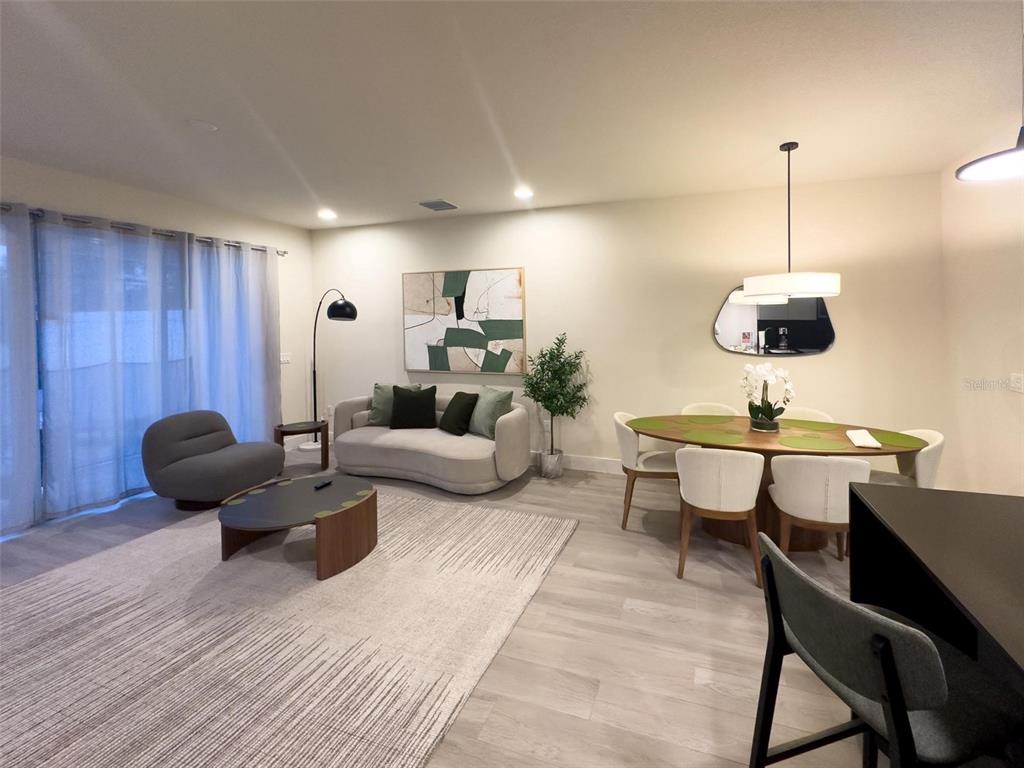 An open-concept living and dining area features light wood-look flooring, modern furniture, and neutral walls — 17422 SERENIDAD BOULEVARD, CLERMONT, FL