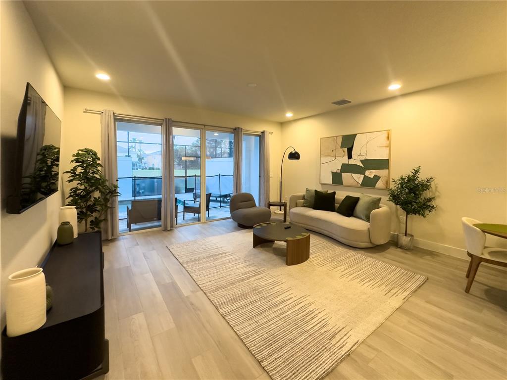 A modern living room features light wood-look flooring, a beige sofa, and sliding glass doors — 17422 SERENIDAD BOULEVARD, CLERMONT, FL