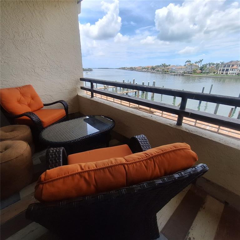 A balcony with wicker chairs, orange cushions, and a glass table overlooking a waterway — 132 1ST STREET E UNIT 101, TIERRA VERDE, FL