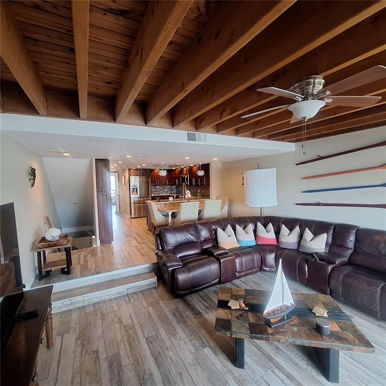 A living room with a sunken floor, wood-beamed ceiling, and an open kitchen in the background — 132 1ST STREET E UNIT 101, TIERRA VERDE, FL
