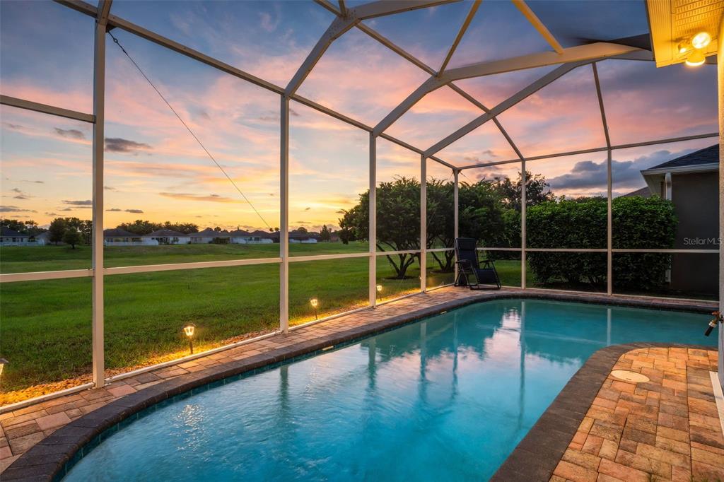 A screened-in swimming pool overlooks a grassy field at sunset — 14912 POTTERTON CIRCLE, HUDSON, FL
