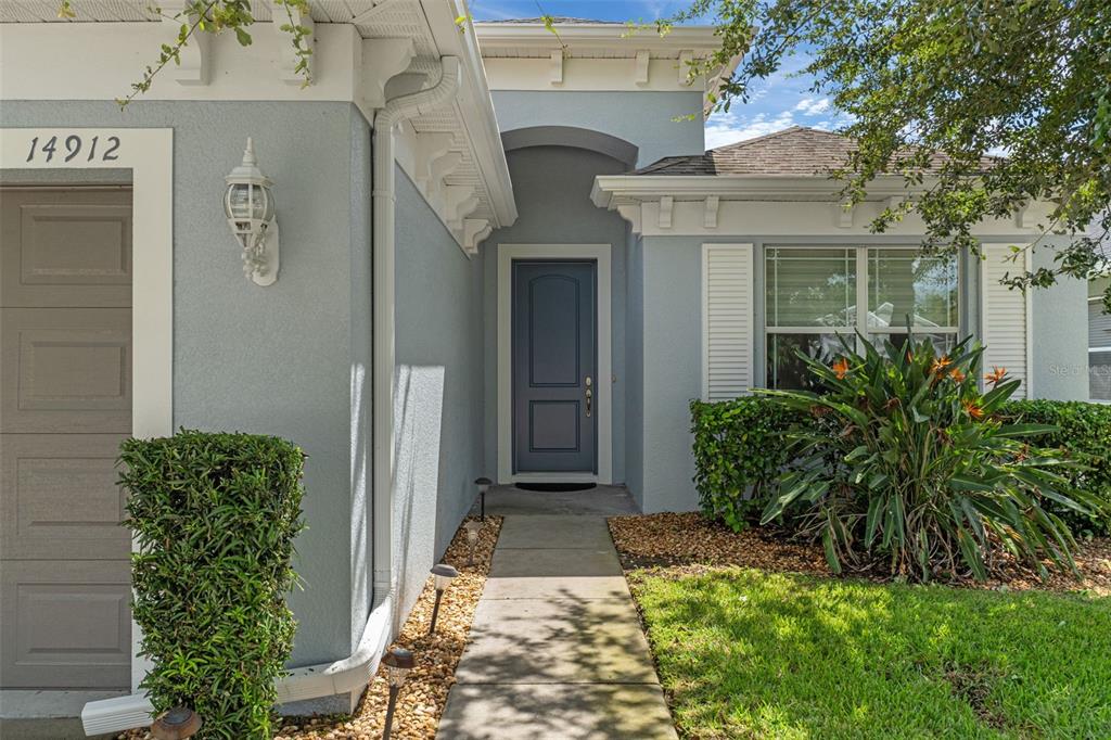 A light blue house exterior features a dark gray front door and a concrete walkway — 14912 POTTERTON CIRCLE, HUDSON, FL