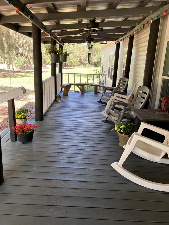 A covered wooden porch features several rocking chairs, ceiling fans, and string lights — 601 PURVIS ROAD, SEVILLE, FL
