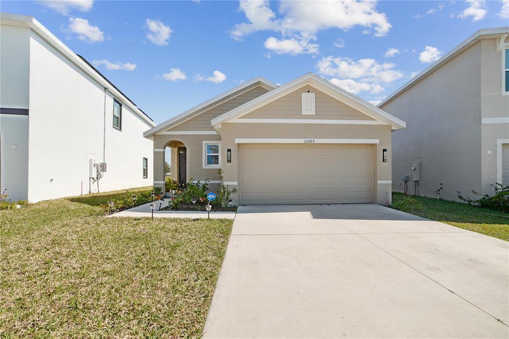 A single-story suburban house with a beige stucco exterior, a two-car garage, and a driveway — 10665 PENNY GALE LOOP, SAN ANTONIO, FL