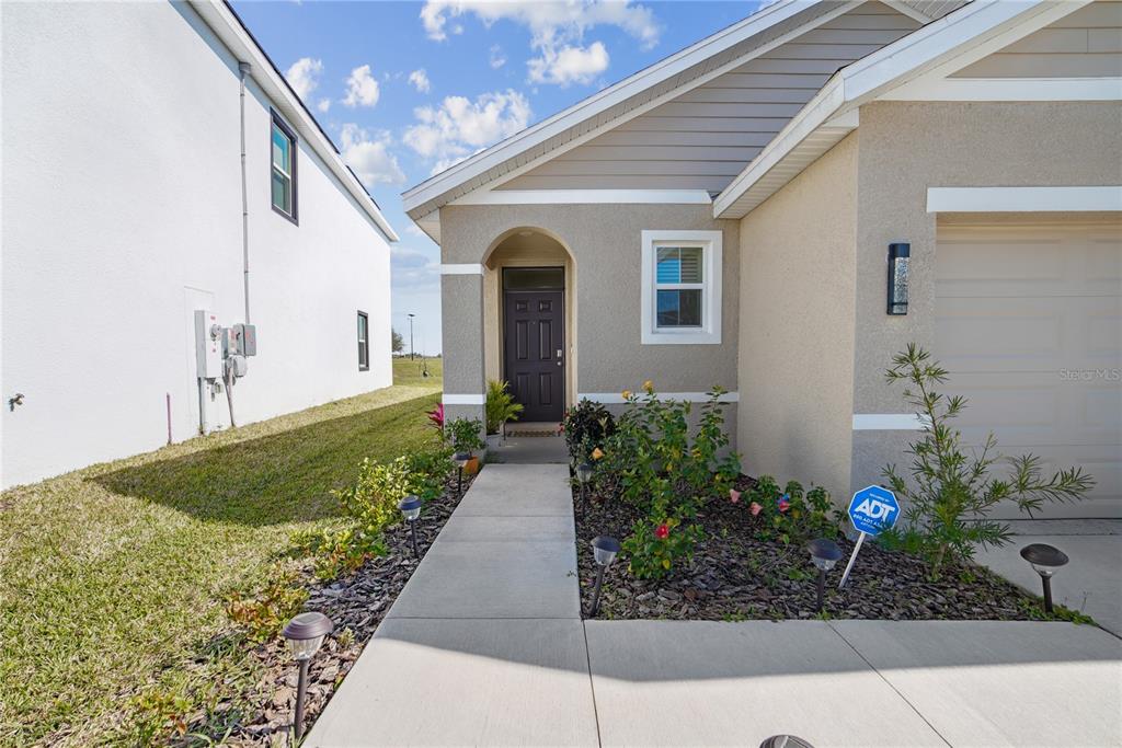 The exterior of a house features a concrete walkway leading to a dark front door — 10665 PENNY GALE LOOP, SAN ANTONIO, FL