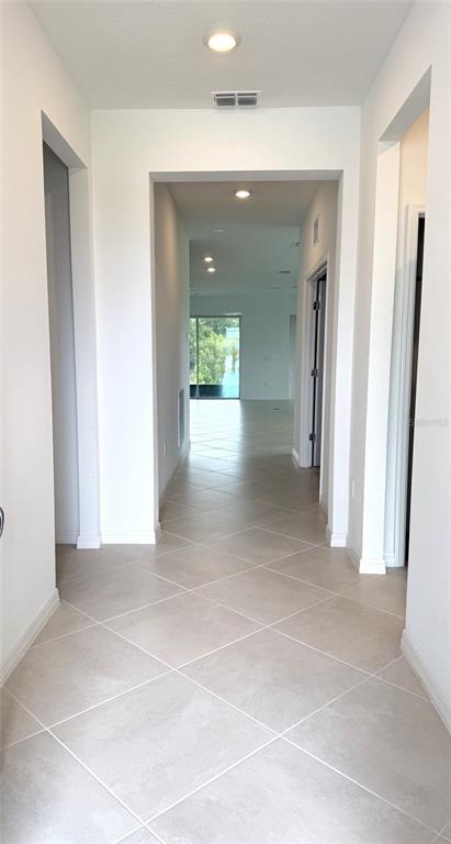 A bright hallway with light-colored tile flooring leads toward an open living area with glass doors — 957 SILVERLAKE BOULEVARD, LAKE ALFRED, FL