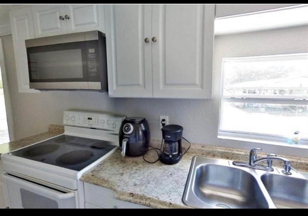 A kitchen features white cabinets, a stainless steel microwave, granite countertops, and a double sink — 3215 TUCKER AVENUE, ST CLOUD, FL