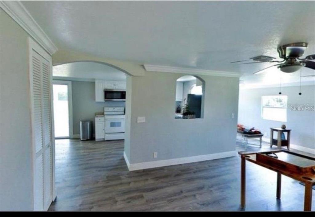 A living area with wood-look flooring leads to an arched opening into a white kitchen — 3215 TUCKER AVENUE, ST CLOUD, FL