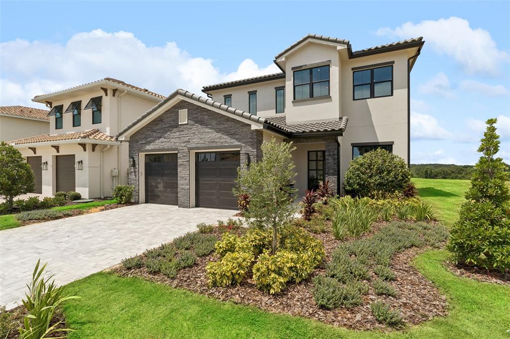 A two-story house with a stone-veneer facade, two garage doors, and a tiled roof — 15825 VETTA DRIVE, BELLA COLLINA, FL