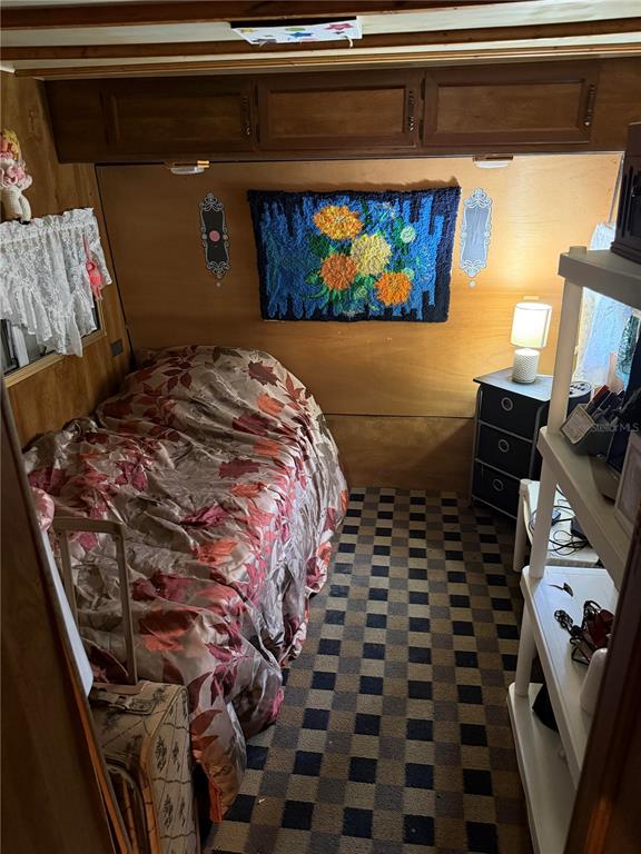 A small bedroom features wood-paneled walls, a floral bedspread, a checkered rug, and wall art — 6521 SE 55TH STREET, OKEECHOBEE, FL