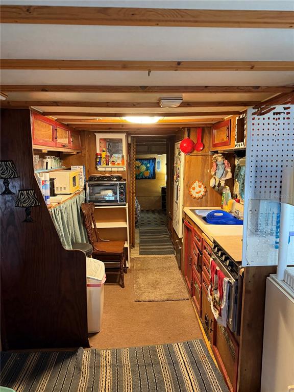 A narrow kitchen features wood-paneled walls, a microwave, a stove, and a small dining chair — 6521 SE 55TH STREET, OKEECHOBEE, FL
