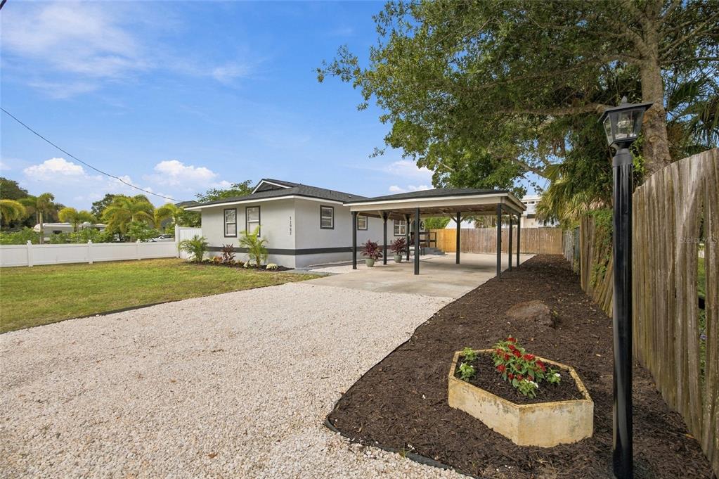 A single-story house with a gravel driveway, carport, and white vinyl fence under a blue sky — 11985 MURRAY AVENUE, SEMINOLE, FL
