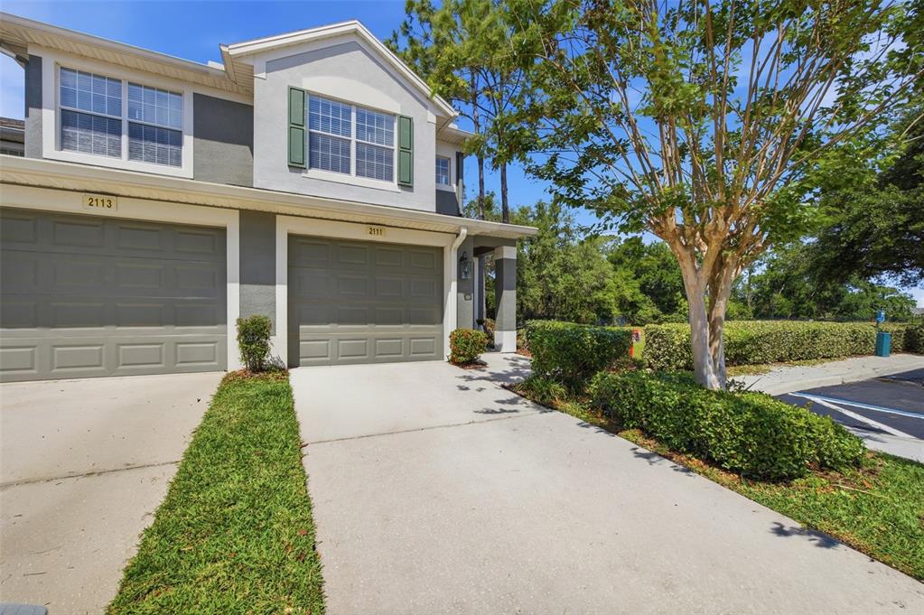 A two-story townhouse exterior features gray siding, green shutters, and two attached garage doors — 2111 RIVER TURIA CIRCLE, RIVERVIEW, FL