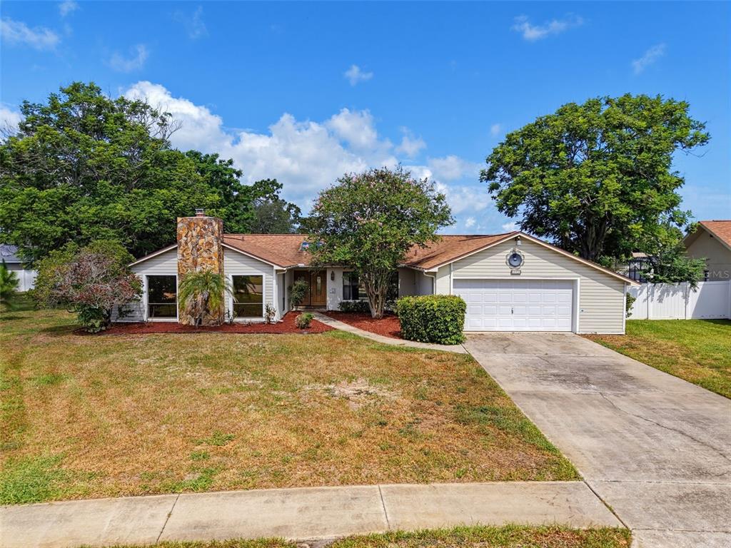 A single-story house with a stone chimney, beige siding, and a two-car garage — 13241 HILLWOOD CIRCLE, HUDSON, FL
