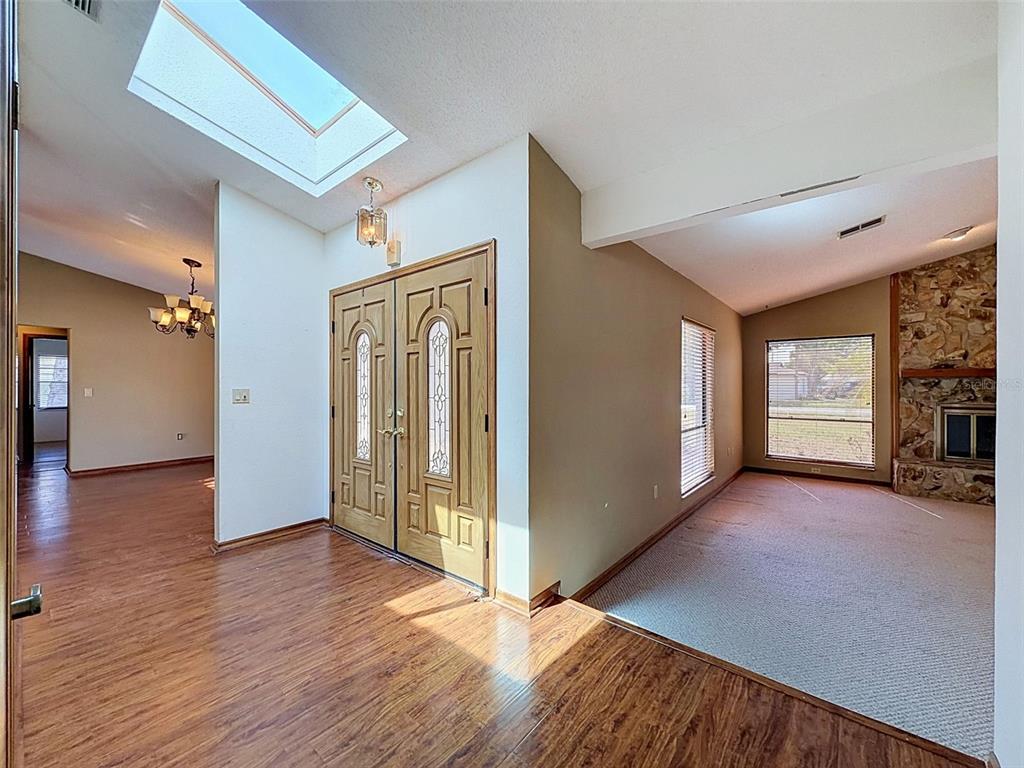 An entryway with wood flooring, a skylight, and double front doors leads into a carpeted living room — 13241 HILLWOOD CIRCLE, HUDSON, FL