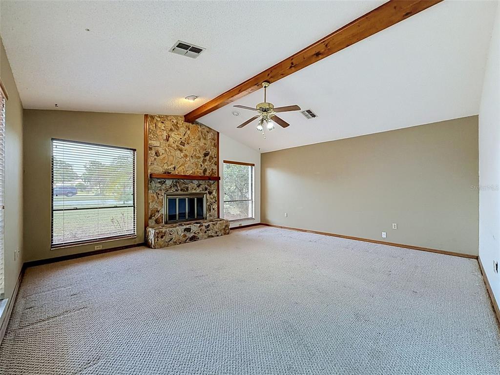 A spacious living room features beige carpet, a stone fireplace, and a vaulted wood-beamed ceiling — 13241 HILLWOOD CIRCLE, HUDSON, FL