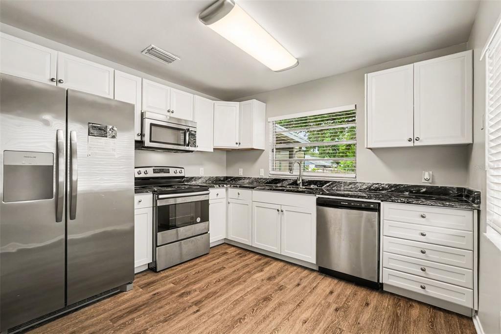 An open-concept living area features wood-look flooring, a vaulted ceiling, and a pass-through kitchen window — 8304 NATCHEZ STREET, TAMPA, FL