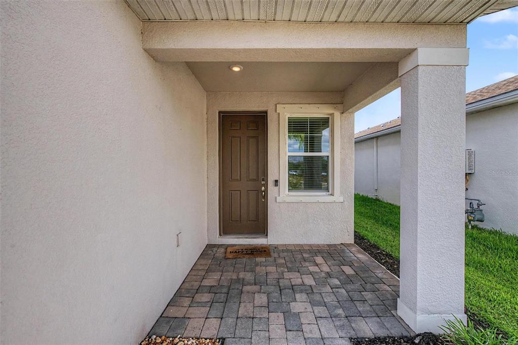 A covered entryway features a brown front door, a window, and a paver patio floor — 5435 BUNGALOW GROVE COURT, PALMETTO, FL