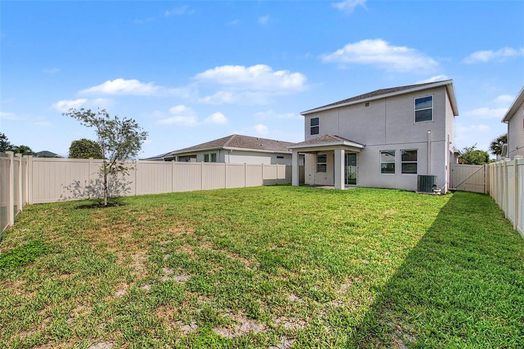 The backyard of a two-story house features a covered patio, lawn, and vinyl fencing — 5435 BUNGALOW GROVE COURT, PALMETTO, FL