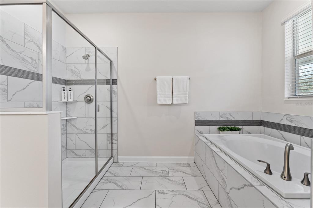 A bathroom features a glass-enclosed shower, a soaking tub, and white marble-style tile flooring — 1577 PLUNKER DRIVE, DAVENPORT, FL