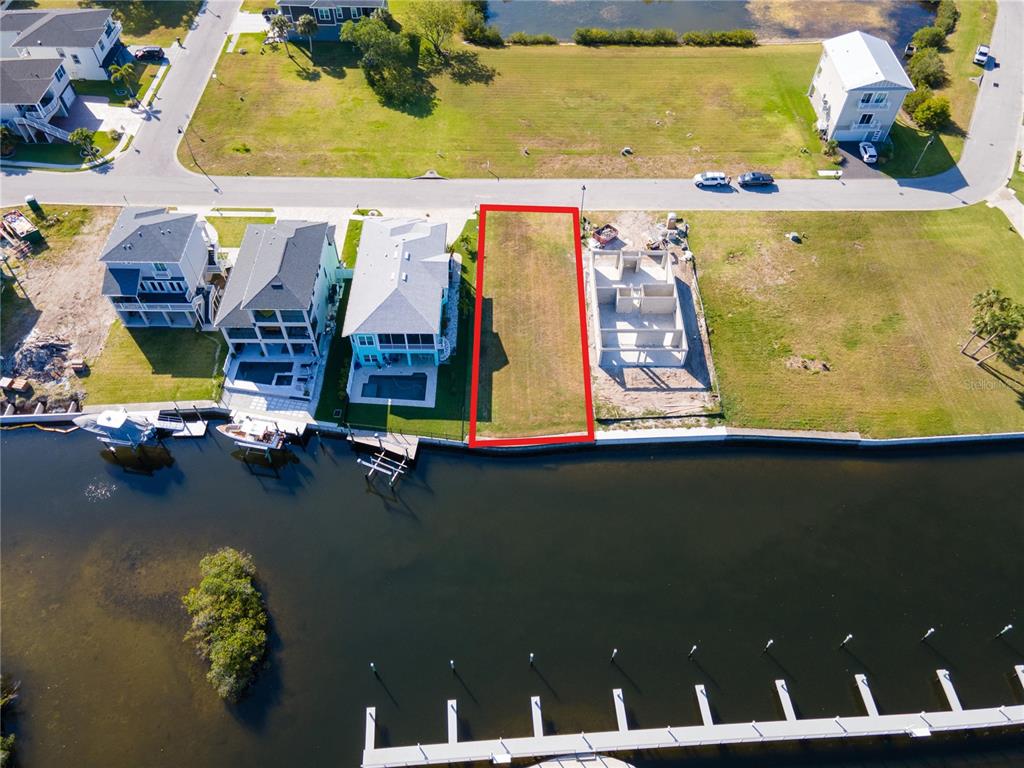 A grassy backyard overlooks a canal with a wooden dock and distant apartment buildings — Lot 7 ELISABETHAN LANE, NEW PORT RICHEY, FL