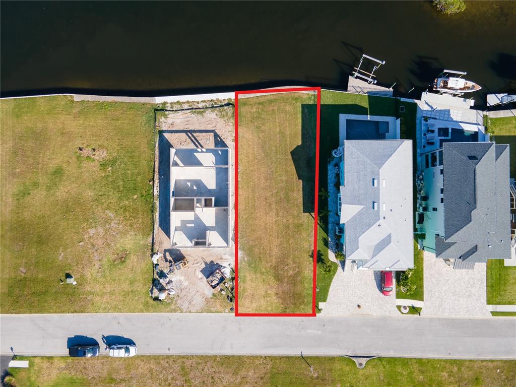 An aerial view shows a vacant waterfront lot outlined in red between two residential properties — Lot 7 ELISABETHAN LANE, NEW PORT RICHEY, FL