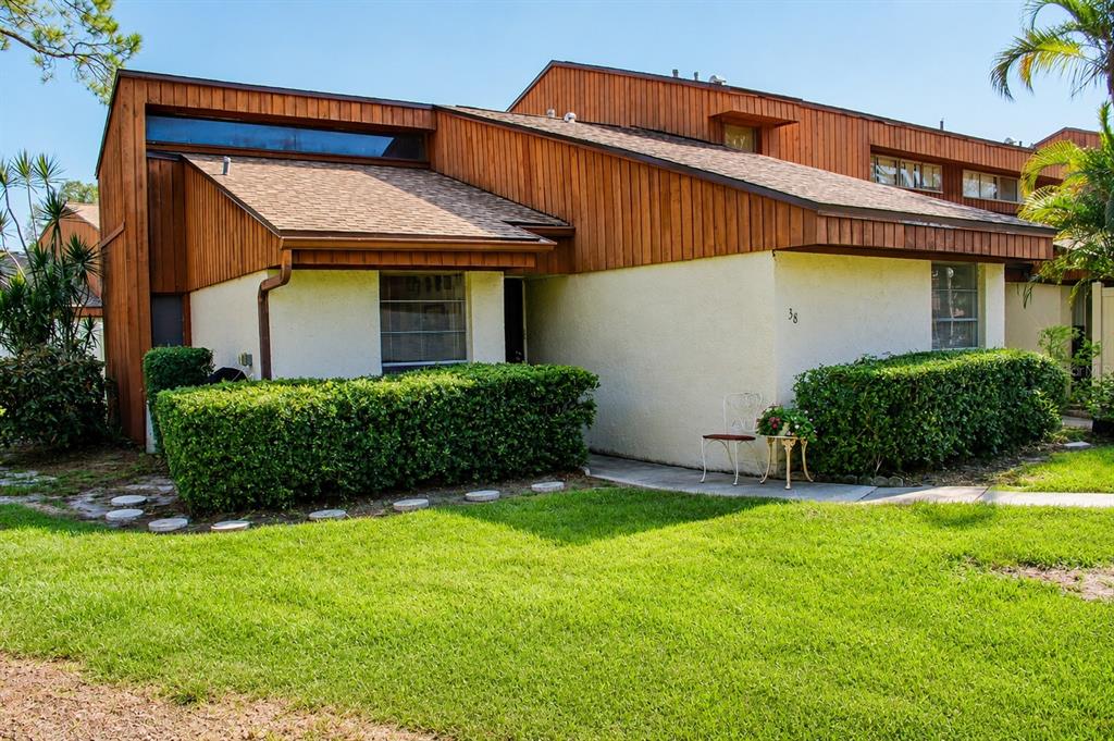 A two-story townhouse with wood siding, stucco walls, and a manicured hedge in front — 2054 SUNSET POINT ROAD UNIT 38, CLEARWATER, FL