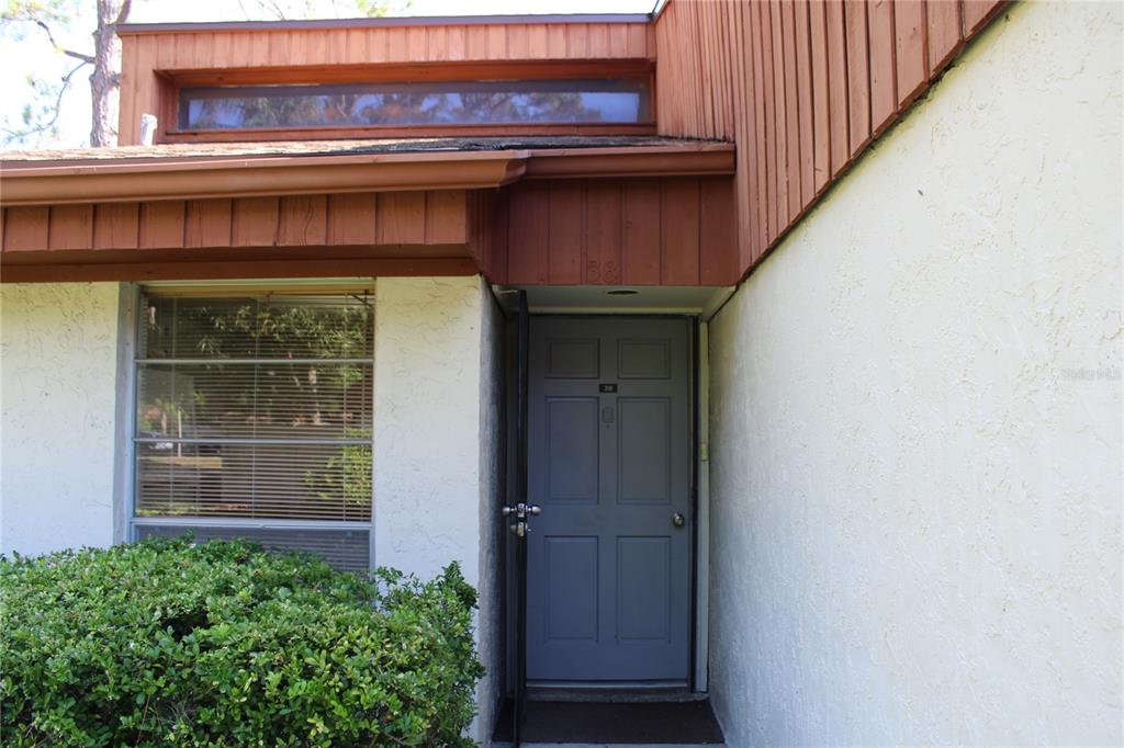 The exterior of a home features a gray front door, a window, and wood siding — 2054 SUNSET POINT ROAD UNIT 38, CLEARWATER, FL