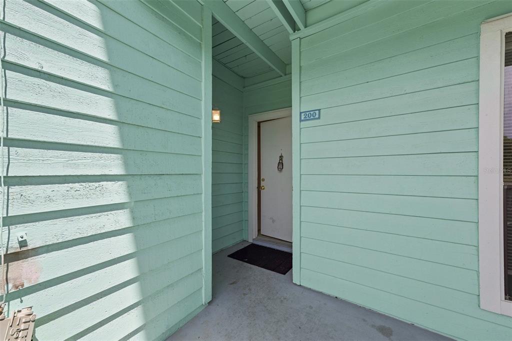 A light green exterior wall with horizontal siding leads to a recessed white front door — 455 ALT 19 S UNIT L200, PALM HARBOR, FL