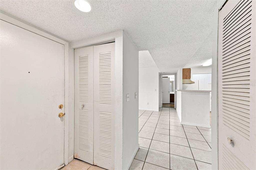 An entryway with white tile floors, louvered closet doors, and a view into the kitchen — 455 ALT 19 S UNIT L200, PALM HARBOR, FL