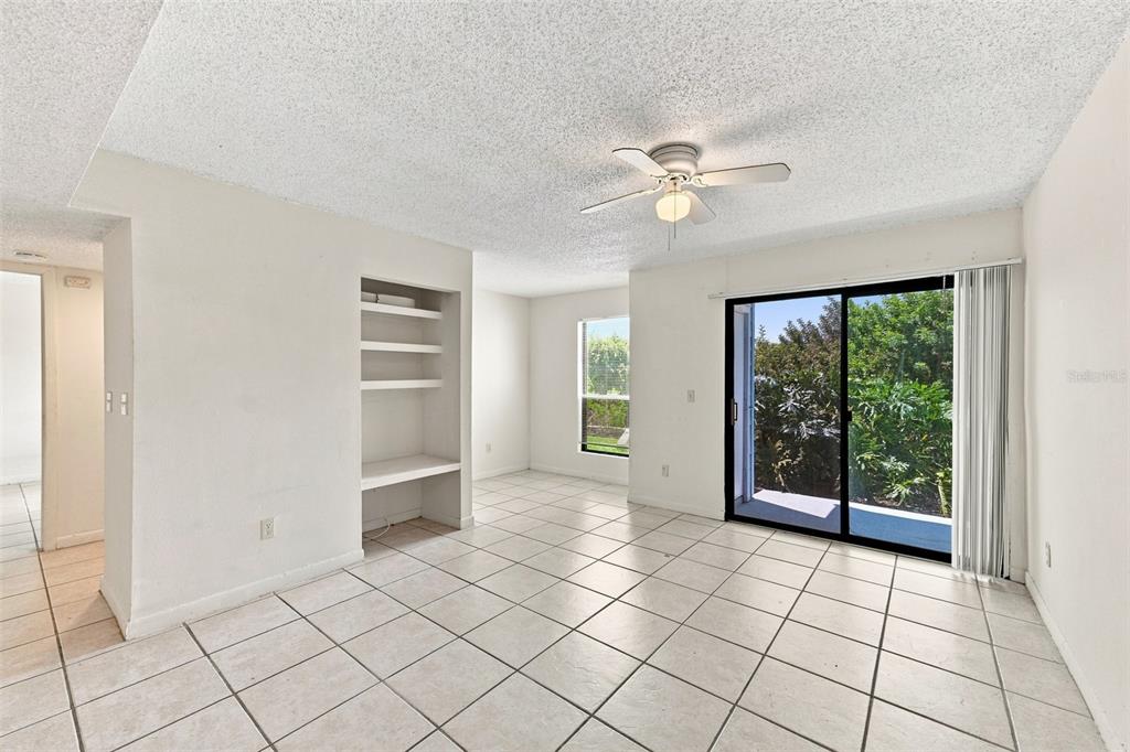 A living room with white tile floors, a ceiling fan, built-in shelves, and sliding glass doors — 455 ALT 19 S UNIT L200, PALM HARBOR, FL