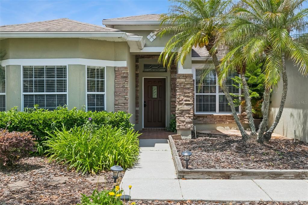 A single-story house exterior features a brown front door, stone accents, and a palm tree — 237 STRATHMORE CIRCLE, KISSIMMEE, FL