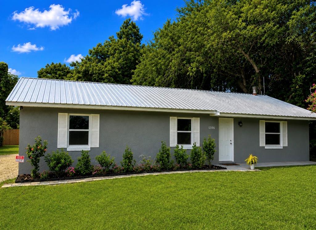 A gray house exterior features a stone walkway, landscaped garden beds, and white window shutters — 12106 SE 74TH TERRACE, BELLEVIEW, FL