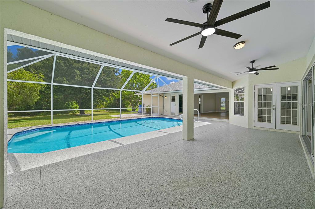 A covered patio with a speckled floor, two ceiling fans, and a screened-in swimming pool — 27334 ORURO DRIVE, PUNTA GORDA, FL