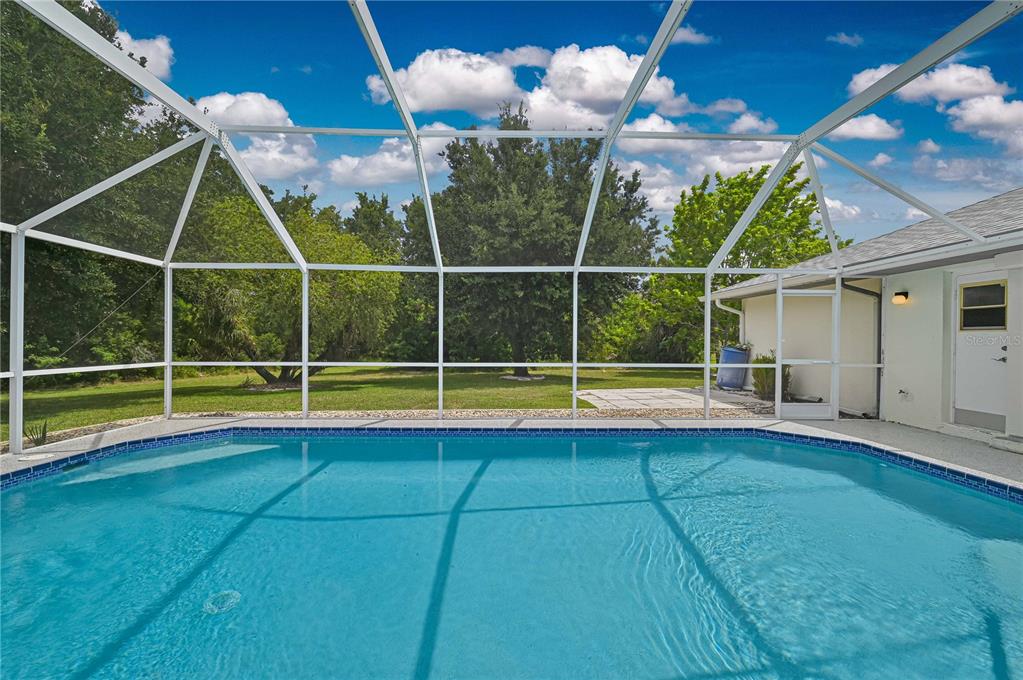 A swimming pool enclosed by a screened lanai overlooks a grassy backyard with mature trees — 27334 ORURO DRIVE, PUNTA GORDA, FL