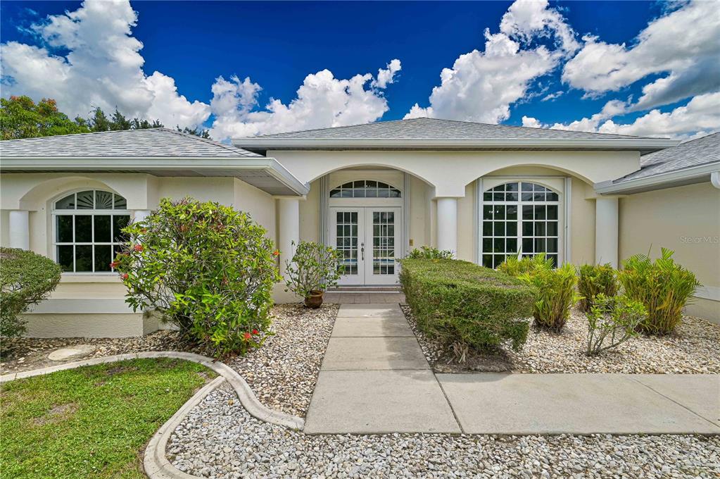 A single-story house with a white stucco facade, arched entryway, and a concrete walkway — 27334 ORURO DRIVE, PUNTA GORDA, FL