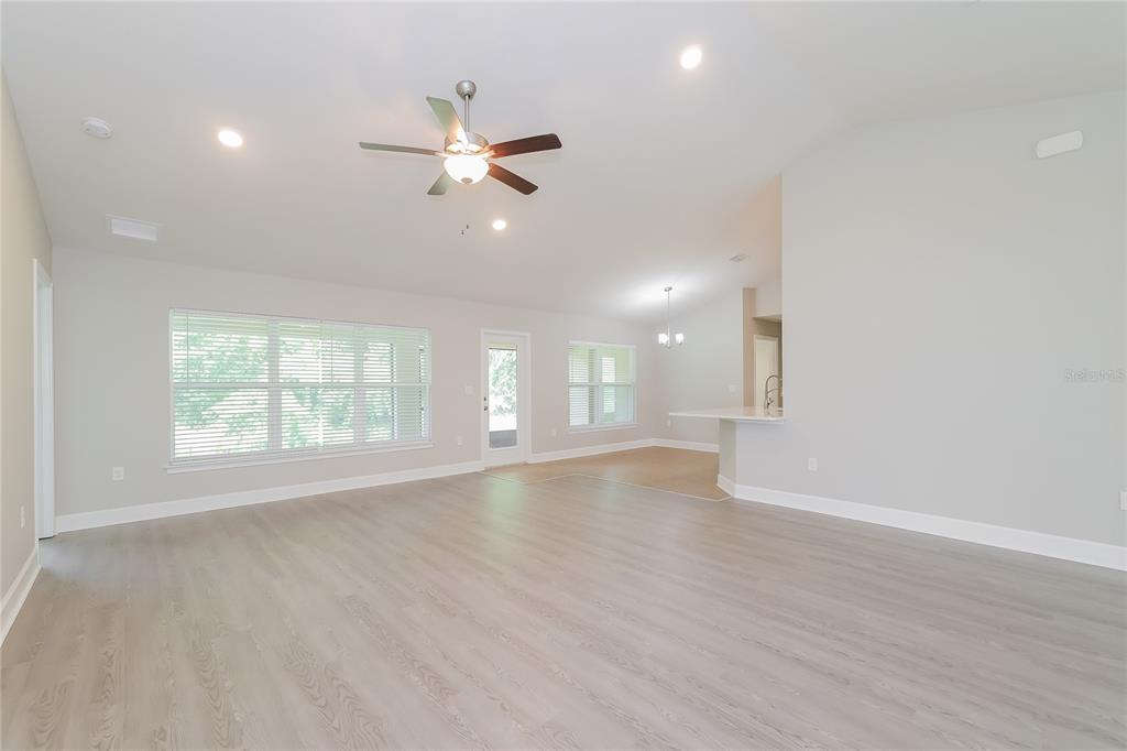 A spacious living room features light wood-look flooring, a ceiling fan, and an open kitchen — 345 CIMARRON COURT, POINCIANA, FL