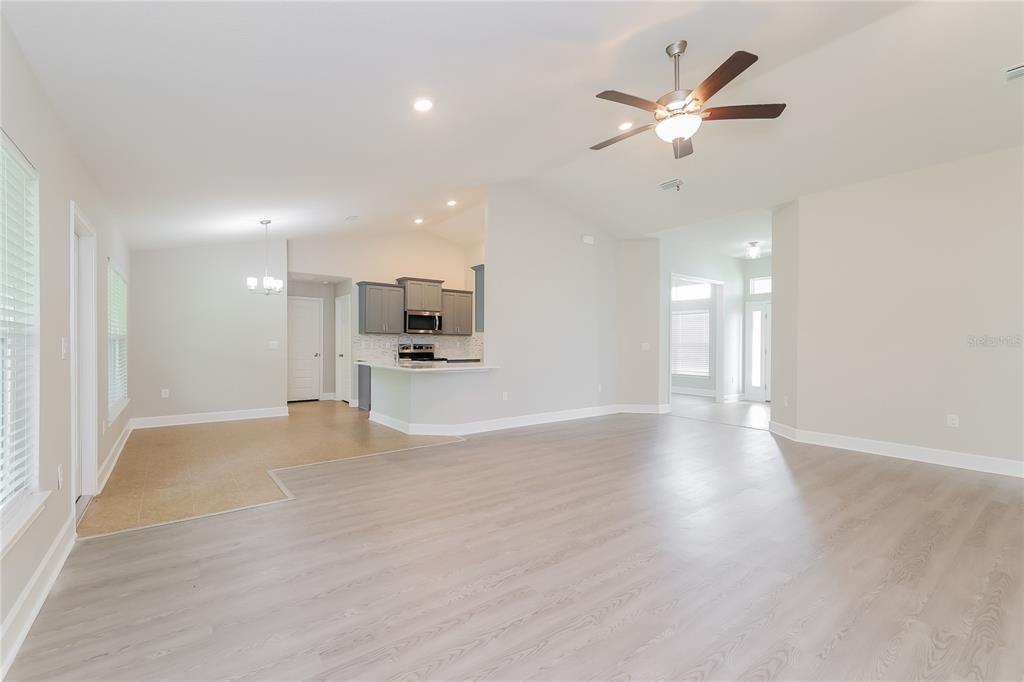 An open-concept living area features light wood-look flooring, a kitchen with gray cabinets, and a ceiling fan — 345 CIMARRON COURT, POINCIANA, FL