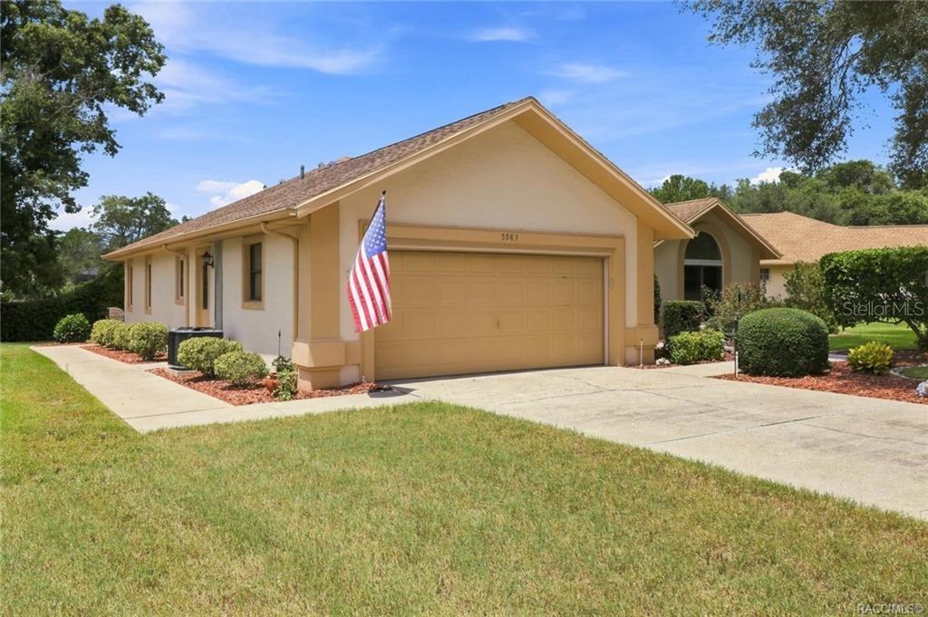 A single-story house with a tan stucco exterior, a two-car garage, and an American flag — 5983 W DOUNERAY LOOP, CRYSTAL RIVER, FL