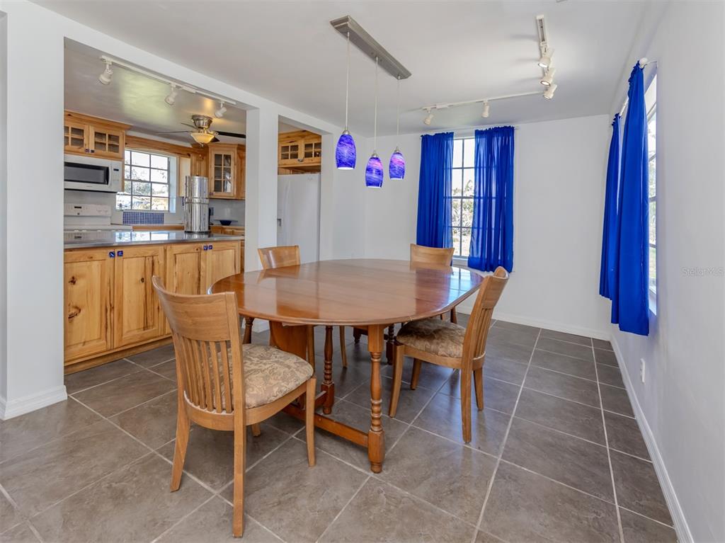A dining room with a wooden table, chairs, blue curtains, and tile flooring — 305 CHAUNCEY AVENUE, BRADENTON, FL