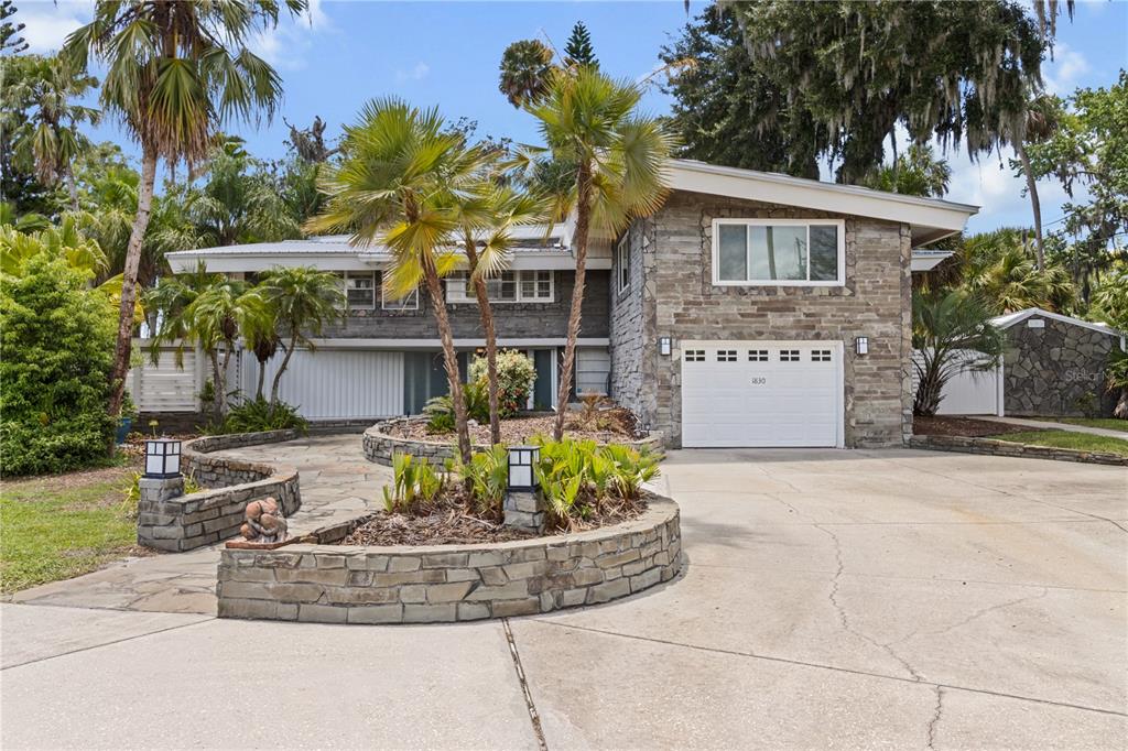 A two-story house with a stone facade, a white garage door, and a curved stone planter — 1830 SE 3RD COURT, CRYSTAL RIVER, FL