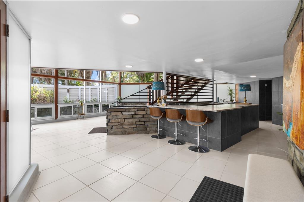 A modern room features a stone-accented bar, three stools, tile flooring, and large glass windows — 1830 SE 3RD COURT, CRYSTAL RIVER, FL