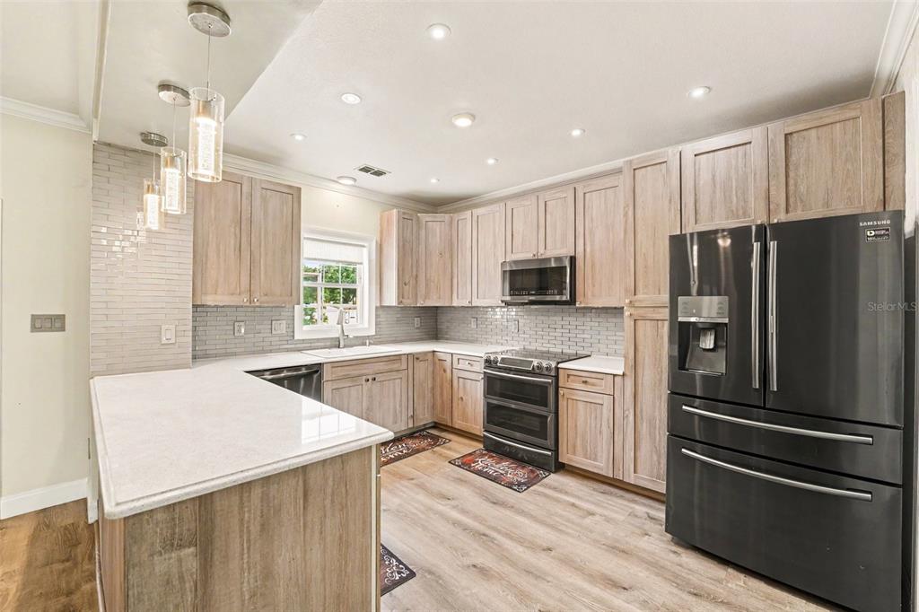 A kitchen with wood-look cabinets, a white countertop, and patterned wallpaper on the walls — 100 SYLVANA COURT, AUBURNDALE, FL