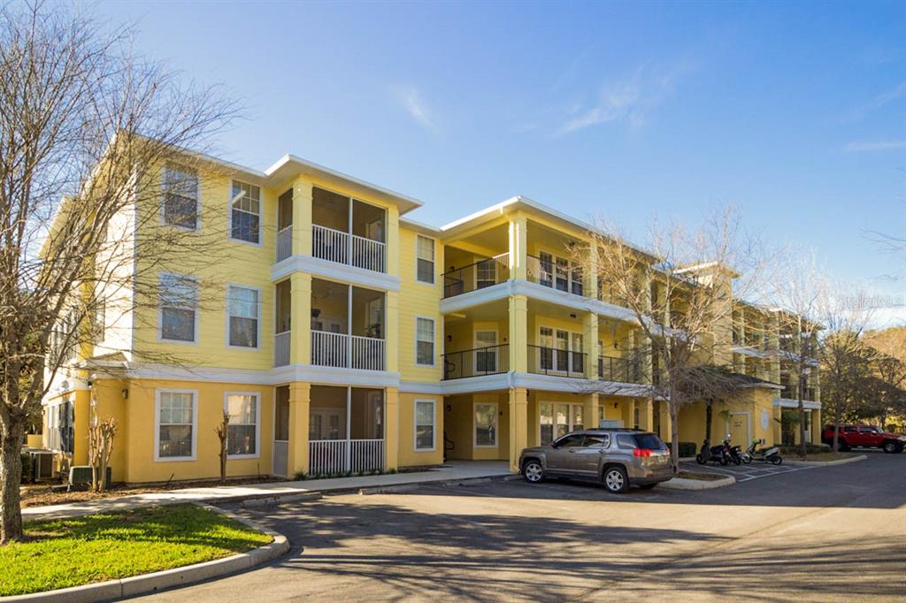 A three-story yellow apartment building with screened balconies and a parking lot in front — 2245 NW 16TH TERRACE UNIT 2245, GAINESVILLE, FL