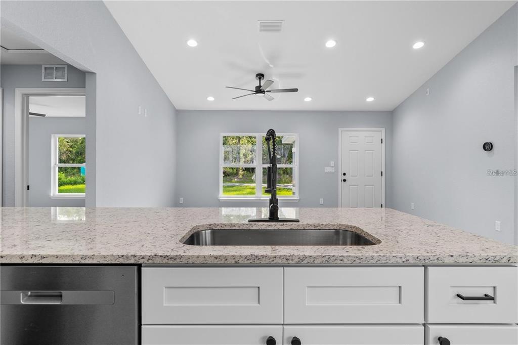 A kitchen island with a stainless steel sink and granite countertop faces a dining area — 13668 SW 112TH STREET, DUNNELLON, FL