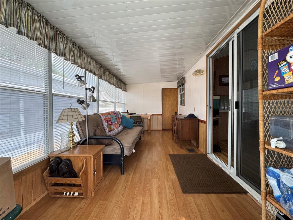 A sunroom features wood-look flooring, a futon, a desk, and large windows with blinds — 4900 BRITNI WAY Lot 70, ZEPHYRHILLS, FL