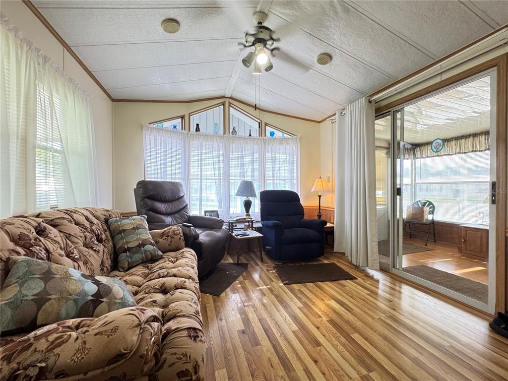 A living room features wood-look flooring, a ceiling fan, a bay window, and sliding glass doors — 4900 BRITNI WAY Lot 70, ZEPHYRHILLS, FL
